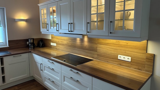 A modern kitchen with white cabinets, a wooden countertop, and a built-in stove.