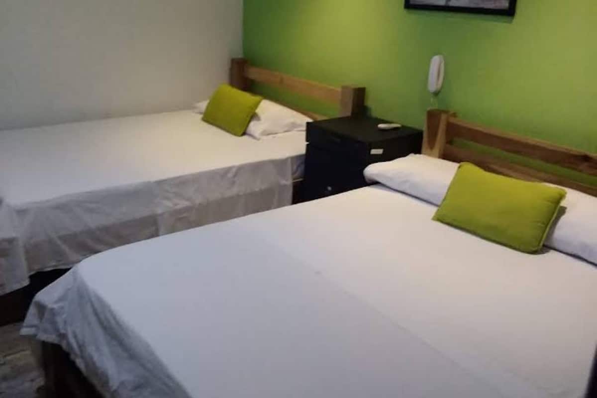 Habitació d'hotel amb dos llits individuals, cadascun amb un coixí verd i roba de llit blanca.