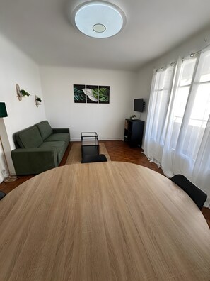 Un soggiorno moderno con un tavolo rotondo in legno, un divano verde, un tavolino in vetro e una televisione a schermo piatto.