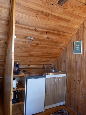 Eine kleine Küche mit Holzwänden, einem Spülbecken, einem kleinen Kühlschrank und einer Kaffeemaschine.