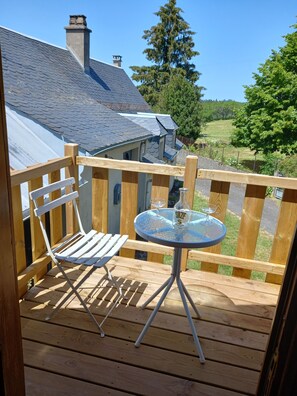 Eine Holzterrasse mit einem tischgestellten Metalltisch und einem weißen Stuhl, mit Blick auf eine Wohngegend mit Häusern und Bäumen.