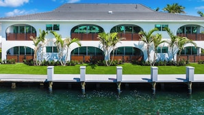 A modern two-story house with a waterfront view, featuring a deck and palm trees. - Villa Arcata: 2BR Boca Water Suite (Boca Raton)