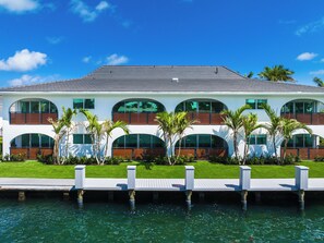Ein modernes, zweistöckiges Haus mit Blick auf das Wasser, mit einer Terrasse und Palmen.