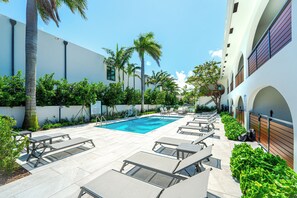 Un espace piscine comprenant des chaises longues, une piscine et un bâtiment doté de fenêtres en arc de cercle.