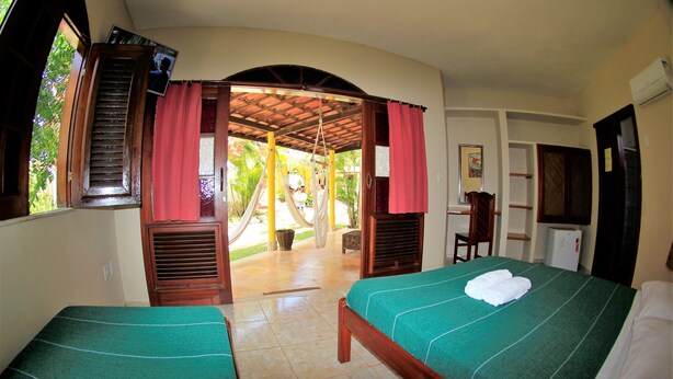 A room with two beds, a desk, a chair, and a view of a garden. - Pousada Paracuru kite Village (Paracuru)