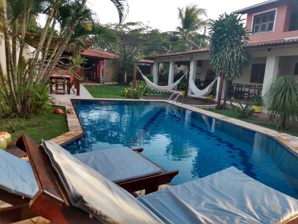 A swimming pool with lounge chairs, a hammock, and a house with a red roof.