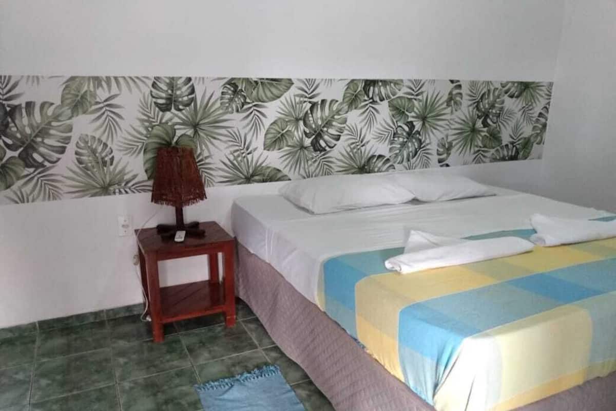 A bedroom with a bed, a nightstand, a lamp, and a tropical leaf-patterned headboard.