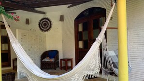 A hammock under a wooden beam, a wicker chair with a cushion, a small wooden table, and a wall with carved designs. - Pousada Paracuru kite Village (Paracuru)