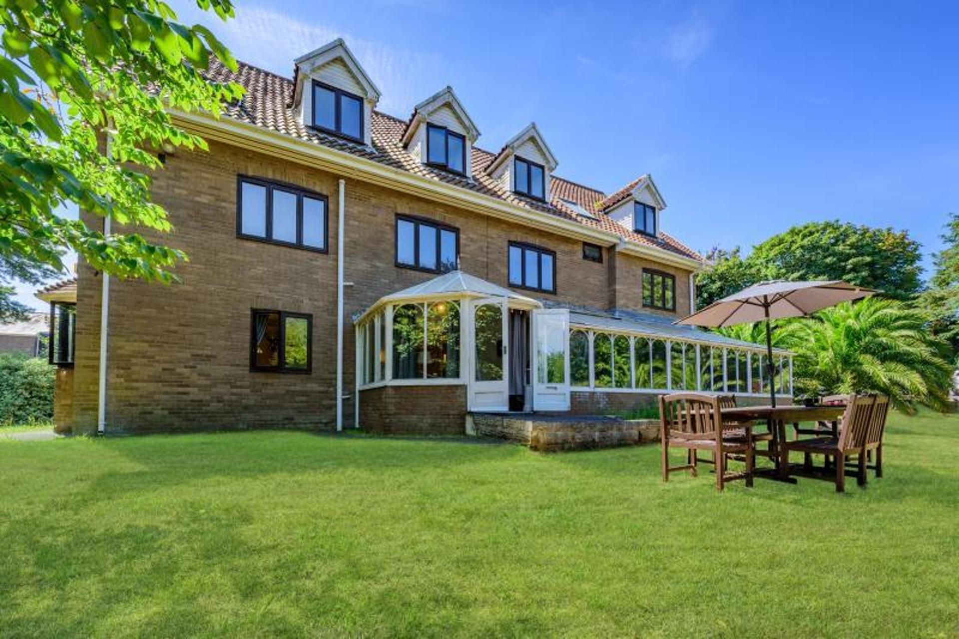 A two-story house with a conservatory, a patio with a table and chairs, and a well-maintained lawn.