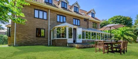 A two-story house with a conservatory, a patio with a table and chairs, and a well-maintained lawn.