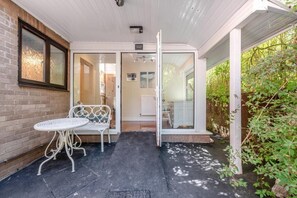 A covered patio area with a white bench and table, a glass door leading to an interior space, and a brick wall. - Apartment - Sleeps 6 - Private Garden (Swansea)