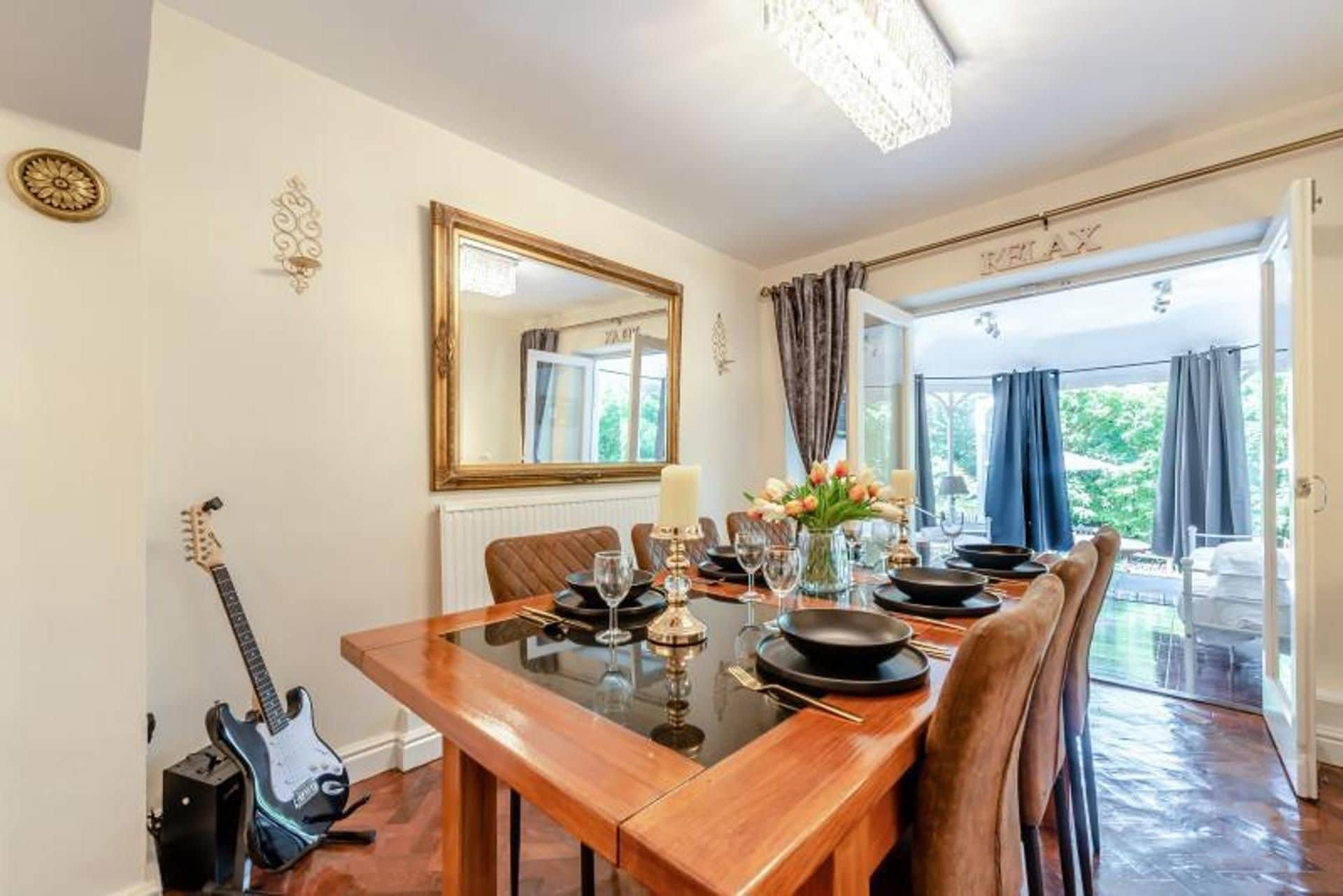 A dining room with a wooden table, chairs, a chandelier, a mirror, and a guitar.