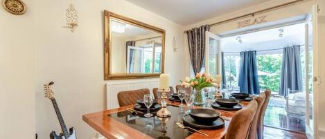 Un comedor con una mesa de madera, sillas, un candelabro, un espejo y una guitarra.