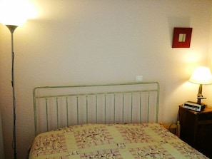 Ein Bett mit Metallkopfteil, einer Nachttischlampe und einer Wandleuchte.