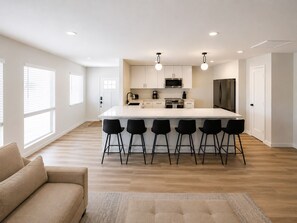 A modern kitchen with a central island, bar stools, and a sofa in a bright room with large windows. - The First Inn Parker Arizona (Parker)