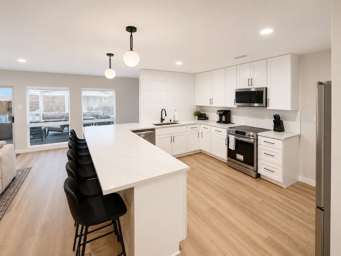 A modern kitchen with white cabinetry, a central island with bar stools, a built-in oven, and a microwave.