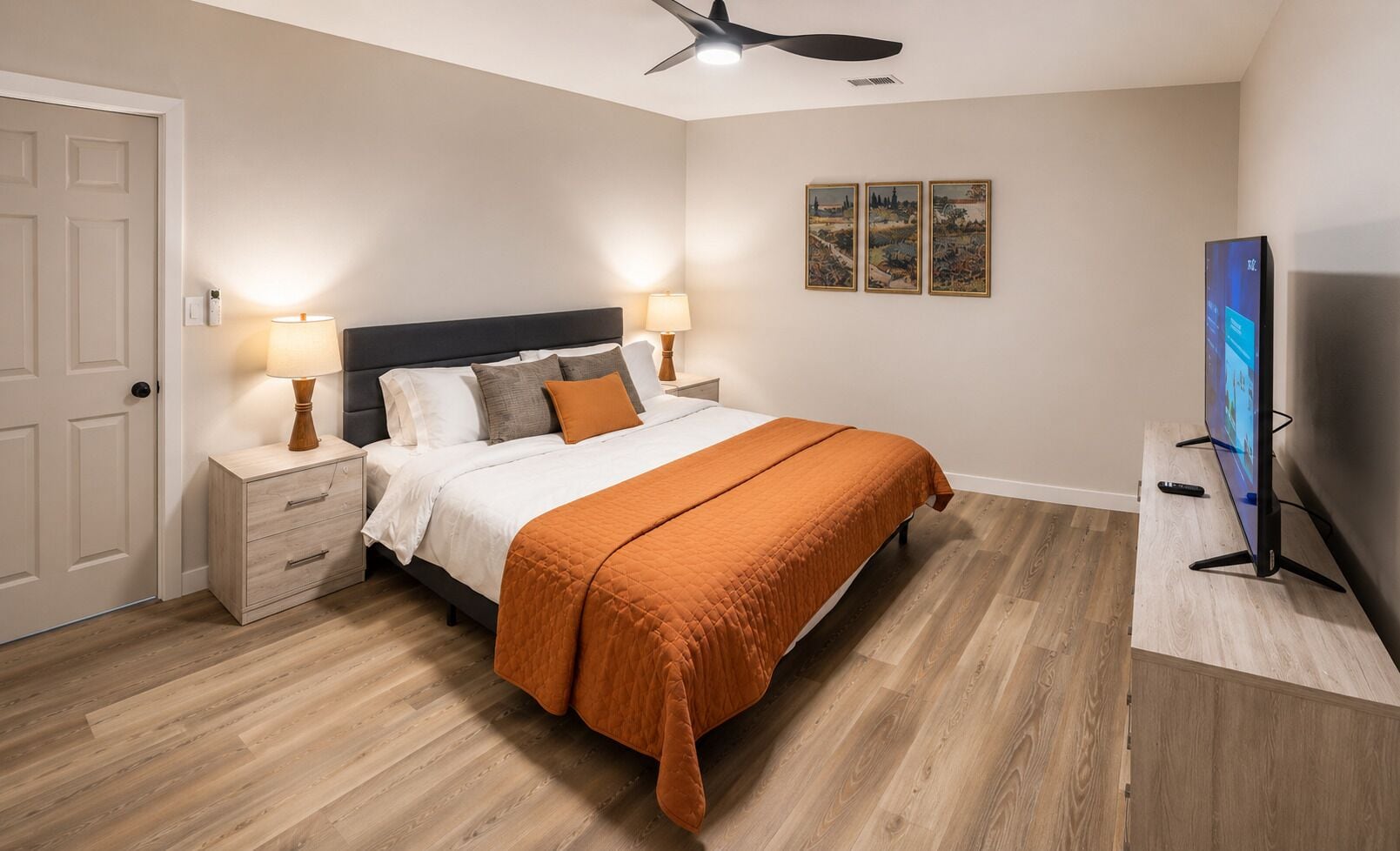A bedroom with a bed, bedside tables, a TV, and artwork on the wall.