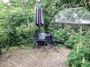 Eine Gartenpatio mit Tisch und Stühlen, einem Sonnenschirm und einem Gewächshaus.