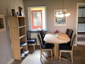 Ein Essbereich mit einem runden Tisch, schwarzen Stühlen, einem Holzregal und einem Fenster mit rotem Rahmen.