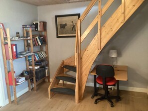 Een compacte kamer met een houten trap, een bureau met stoel en een boekenplank vol boeken.