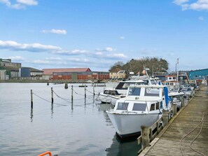 A marina with boats docked, a wooden pier, and industrial buildings in the background. - 6 Person Holiday Home in Bandholm (Bandholm)
