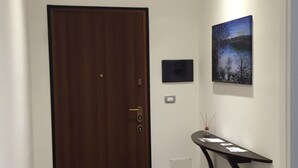 A hallway with a wooden door, a wall-mounted picture, and a small table with papers. - Room 'Camera Matrimoniale Monica' with Wi-Fi and Air Conditioning (Alghero)