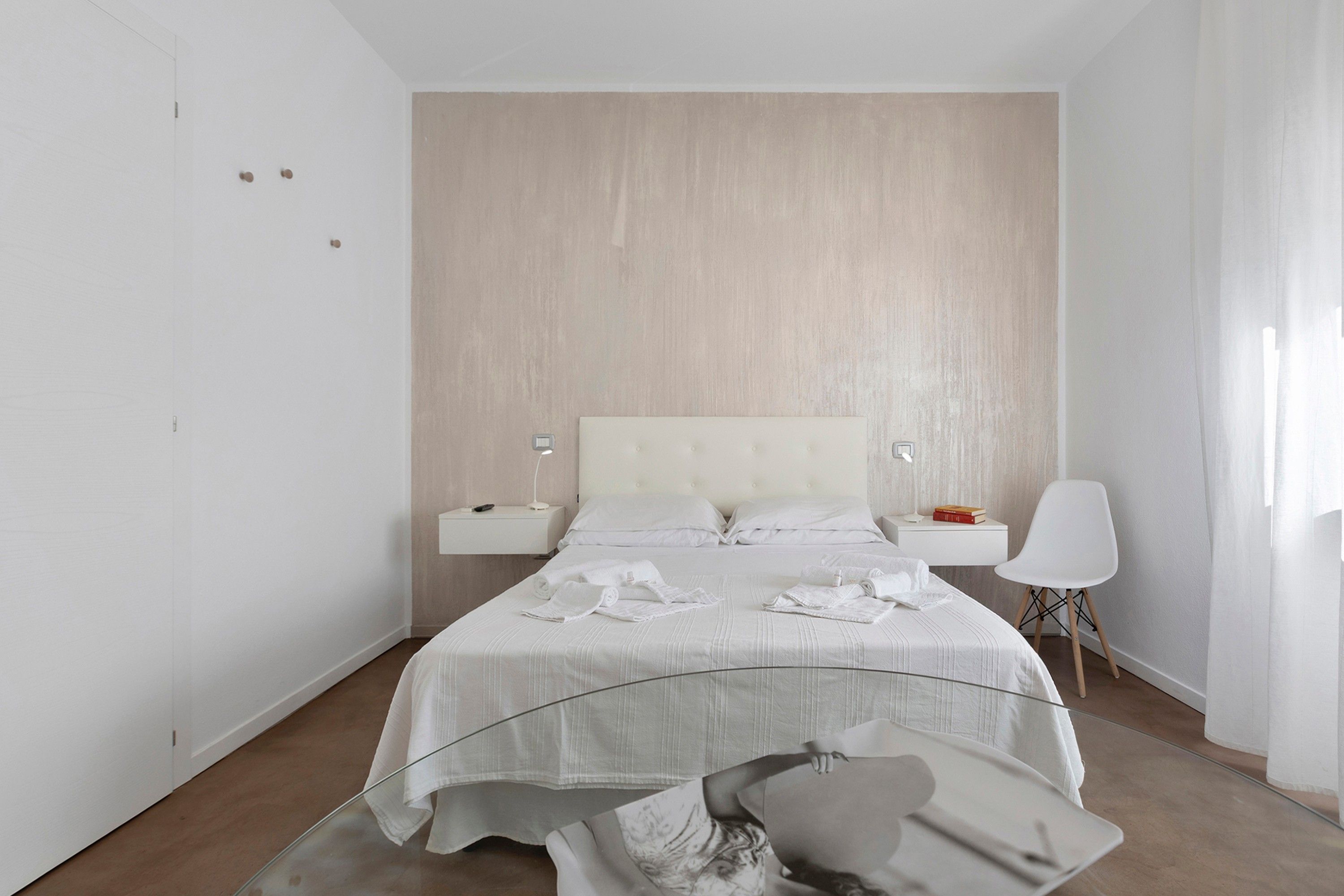 A modern hotel room with a large bed, a bedside table, a chair, and a nightstand.