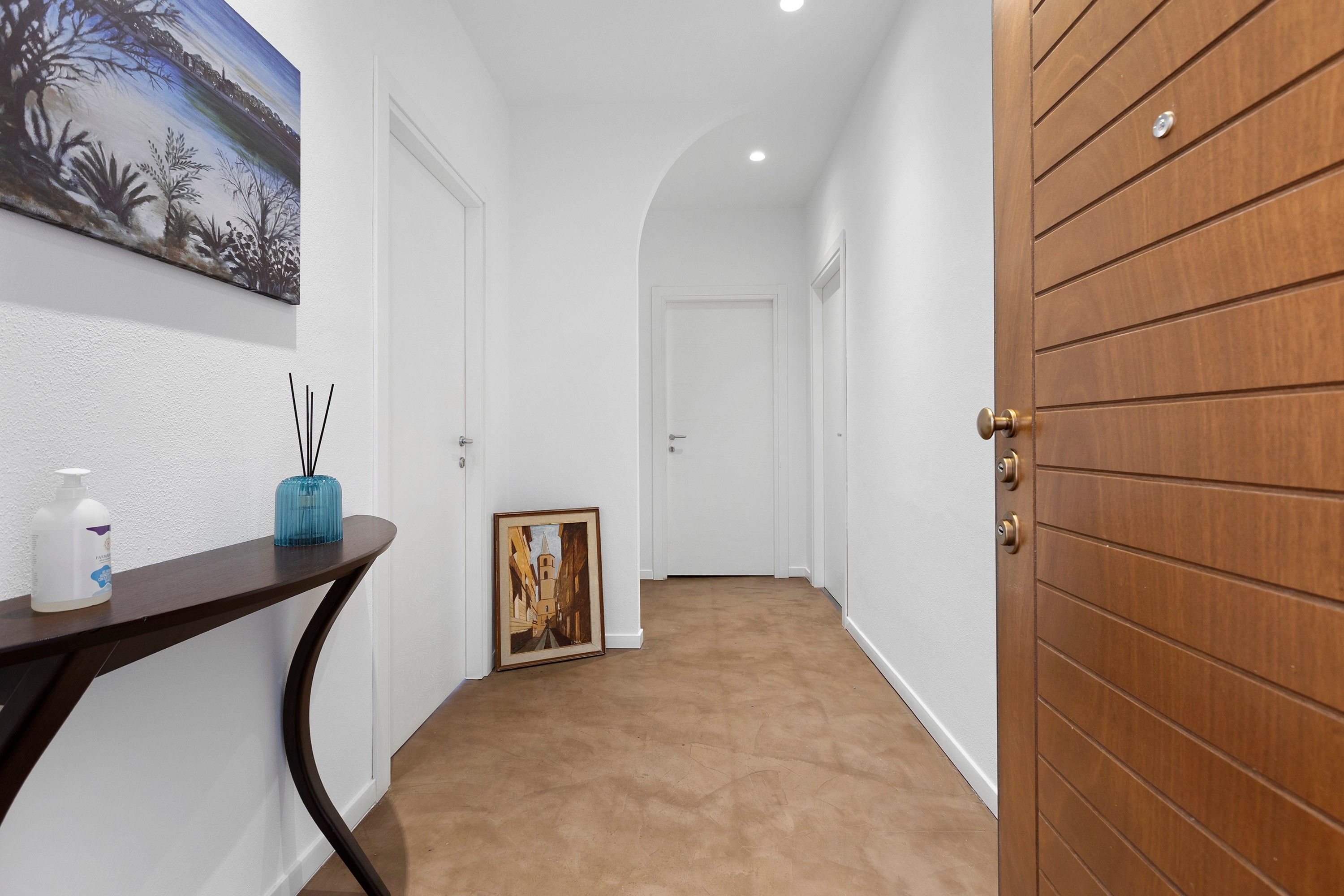 A hallway with a wooden door, a framed picture, and a small table with a bottle and reed diffuser.