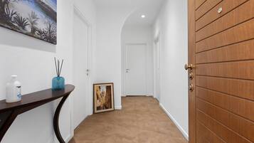 A hallway with a wooden door, a framed picture, and a small table with a bottle and reed diffuser.