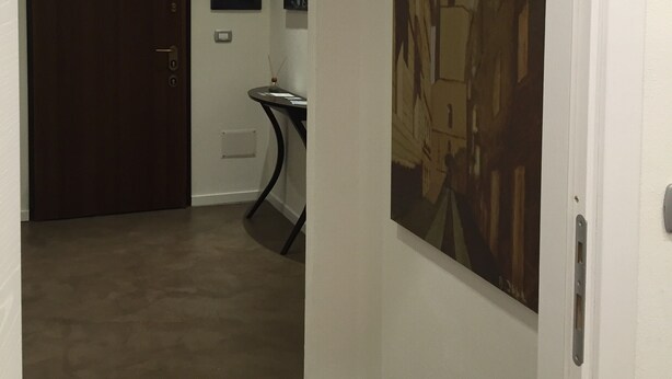 A hallway with a dark wooden door, a small table with a candle, and a painting of a building on the wall. - Room 'Camera Matrimoniale Monica' with Wi-Fi and Air Conditioning (Alghero)