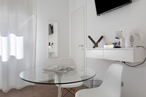 Et moderne værelse med et glasbord, hvide stole, et ophængt tv og et hvidt skab med hårde hvidevarer.