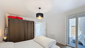 Ein modernes Hotelzimmer mit Bett, Schrank, einem roten Regenschirm, einer Pendelleuchte und Blick ins Freie.