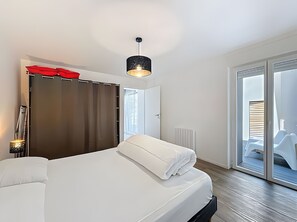 Moderni hotellihuone, jossa on sänky, vaatekaappi, punainen sateenvarjo, riippuvalaisin ja näkymä ulos.