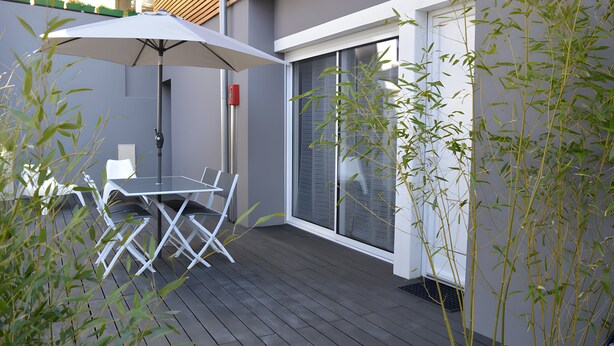 Eine Terrasse mit Tisch und Stühlen, einem weißen Sonnenschirm und Bambuspflanzen.
