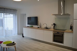 Moderni keittiö, jossa on sisäänrakennettu uuni, ruostumattomasta teräksestä valmistettu liesituuletin, litteänäyttöinen televisio ja ikkuna, jossa on sälekaihtimet.