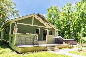 A green building with a porch, outdoor seating, and a grill.