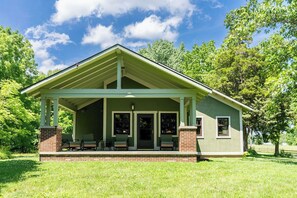 A single-story house with a porch, brick foundation, and green siding.