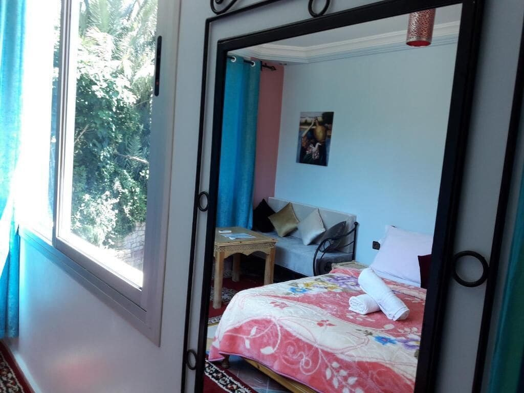 A bedroom with a bed, a small table, a sofa, and a window with curtains.