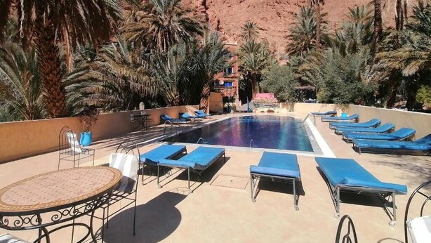Zona de piscina con sillones de descanso, palmeras y montañas al fondo.