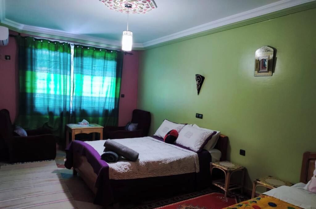 Une pièce comprenant un lit, une chaise, une petite table et un luminaire fixé au mur.