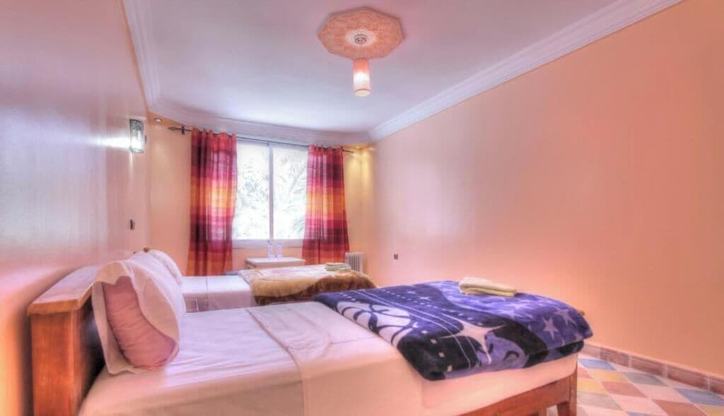 A bedroom with two beds, a window with curtains, a ceiling light, and a tiled floor.
