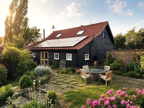 Ein schwarzes Haus mit rotem Ziegeldach, ein Garten mit einem Kiesweg und ein Tisch mit Stühlen.