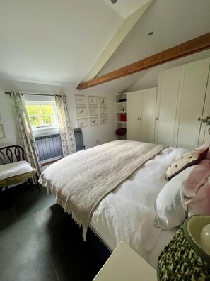 Quarto com cama, poltrona, janela com cortinas, parede com quadros e guarda-roupa.