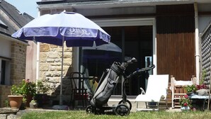 A stroller, a baby carrier, and a baby seat outside a house with a stone wall and a wooden fence.