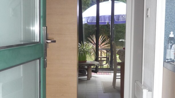A hallway with a glass door, a wooden door, a tiled floor, a ceiling fan, a table with chairs, and a view of the outdoors.