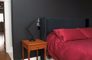 A bedroom with a dark headboard, a wooden bedside table with a lamp, and a red bedspread.