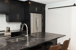 Una cocina moderna con armarios oscuros, electrodomésticos de acero inoxidable, una encimera negra y un lavamanos integrado.