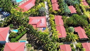 Ett flygbildsbild av ett semesterområde med flera byggnader, en swimmingpool och frodig grönska.