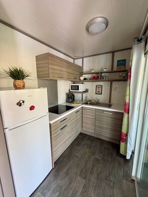 A compact kitchen with a white refrigerator, a microwave, a coffee maker, and wooden cabinets.