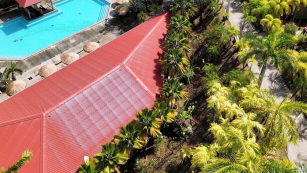Ett semesterhotell med en swimmingpool, byggnader med röda tak och utsikt över havet.
